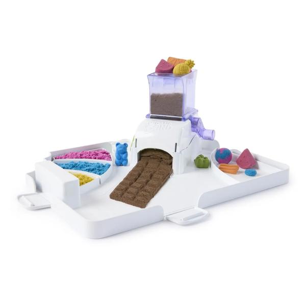 Creeaza si personalizeaza bomboane si dulciuri cu Statia de Dulciuri Kinetic Sand Acest set de joaca adorabil ii invita pe tinerii cofetari sa isi faca propriile dulciuri din nisip Cu un total de 450g de nisip roz galben turcoaz si maro copiii pot amesteca culorile pentru a modela viermisori gumati sau batoane de ciocolata Masina de bomboane face distractia si mai mare incarca nisipul roteste manivela si priveste cum apar deliciile Acest proces interactiv dezvolta abilitatile motorii 