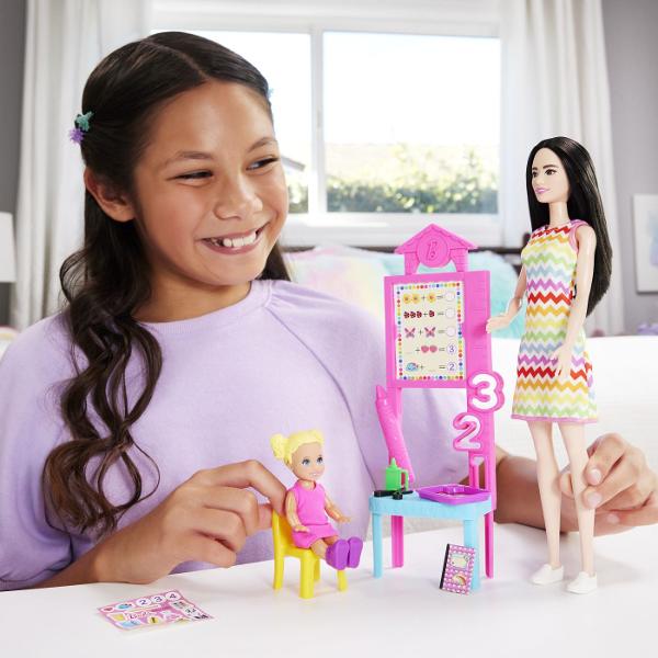 Descopera setul de joaca Barbie Profesor perfect pentru copiii care isi doresc sa exploreze lumea educatiei prin joaca Acest set ofera oportunitatea de a recrea lectii interesante si de a invata prin scenarii interactive Setul include o papusa Barbie bruneta profesoara imbracata intr-o rochie colorata cu model vesel gata sa predea lectii captivante Sala de clasa este echipata cu o tabla interactiva materiale educative si accesorii specifice care completeaza experienta de invatare De 