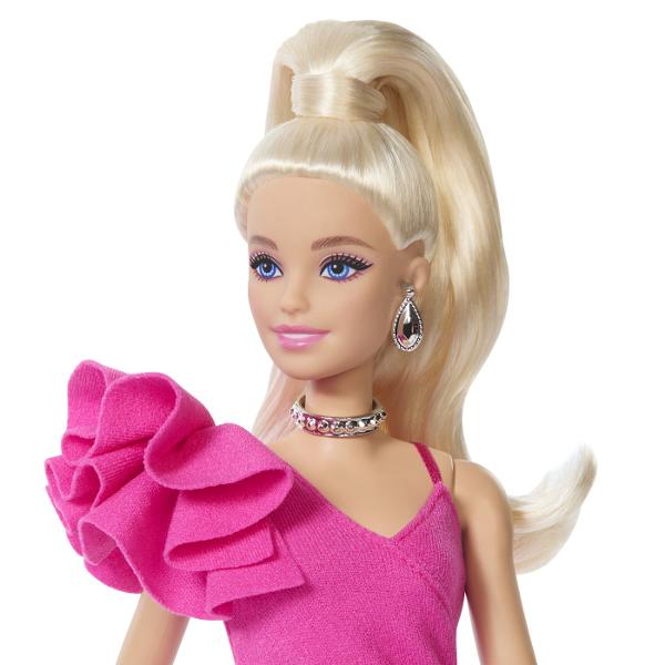 Papusa Barbie Deluxe Style impresioneaza printr-o tinuta eleganta si moderna potrivita pentru momente speciale si joaca inspirata de lumea modei Barbie poarta o rochie roz intens cu croiala asimetrica si detalii drapate completata de dresuri cu model si accesorii stralucitoare Parul blond lung coafat intr-o coada inalta completeaza look-ul sofisticat iar cerceii colierul bratara si poseta argintie adauga un plus de stil Papusa este articulata si poate fi pozitionata in diferite 